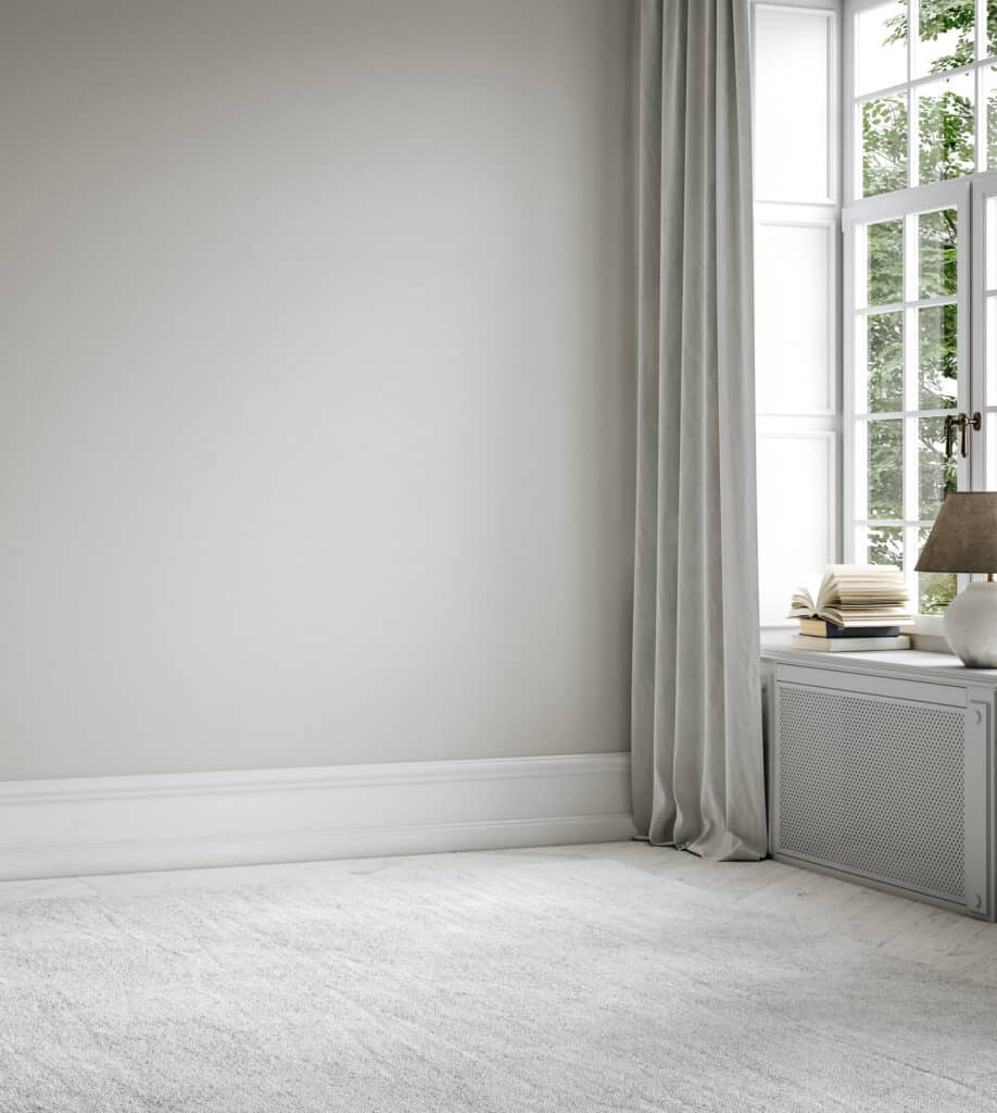 Intérieur moderne et lumineux : mur gris clair, grande fenêtre avec verdure, rideaux drapés, tapis moelleux, cache-radiateur avec livres et lampe.