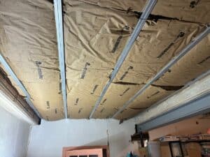 Plafond en cours de rénovation, isolant Knauf Insulation avec EcoSe fixé par des rails métalliques, montrant des zones déchirées.