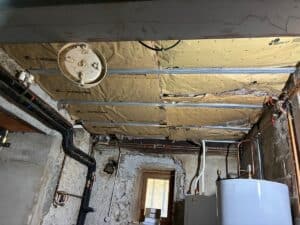 Plafond de sous-sol en cours d'isolation avec laine minérale Knauf Insulation, tuyauterie visible et chauffe-eau.