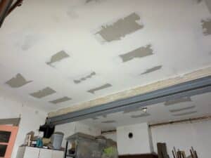 Plafond en plaques de plâtre avec enduit frais sur les joints et têtes de vis, travaux de rénovation en cours, poutre métallique visible.
