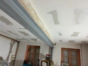 Plafond en cours de rénovation avec plaques de plâtre jointoyées, poutre métallique grise apparente et moulure décrépite.